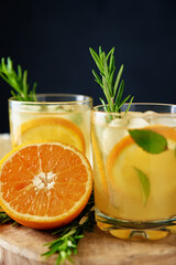 Homemade lemonade with orange and rosemary, Glass of summer coctail on dark background, Citrus detox water for refreshing in hot summer day