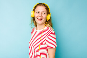 Young caucasian woman wearing headphones isolated on blue background looks aside smiling, cheerful and pleasant.