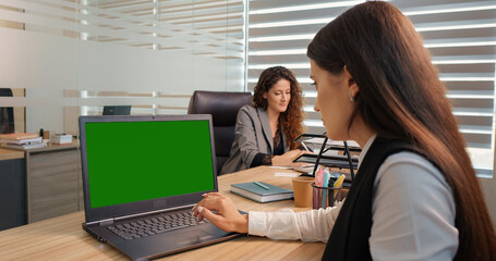 Businessman working on a laptop with green screen on background colleague discussing details. Modern office.