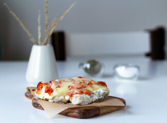 Pork with tomatoes and cheese sauce on parchment paper on a wooden board on a white table.