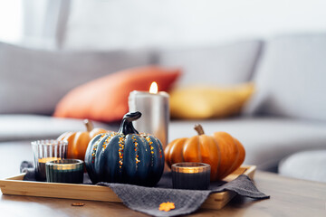Autumn cozy mood composition for hygge home decor. Orange and gray pumpkins , burning candles on the tray with gray napkin on the coffee table in the living room. Selective focus. Copy space.