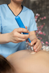 Cropped photo of masseuse doctor applying silicone pump to vacuum plastic cups to pump out air on bare back of woman.