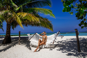 Beautiful sexy tanned woman in golden bikini on Maldives island. Young glamour girl is posing on...