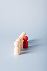 Selective focus on a red wooden figure that stands apart from other identical figures. The concept...