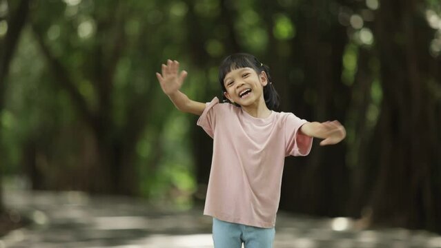 Portrait Thai Asian kid girl, age 5 to 7 years old, pretty and cute. and healthy Running and playing in the outdoor park happily, joyfully and cheerfully smiling The background is green trees.
