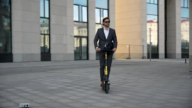 Caucasian businessman in formal wear suit riding electric scooter to work in city