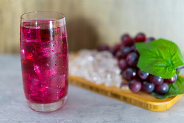 Refreshing a glass of grape juice with ice cubes on wooden tray