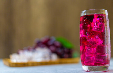 Refreshing a glass of grape juice with ice cubes on wooden tray