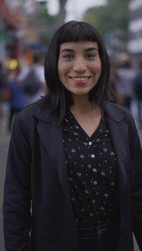 Happy woman with indigenous traits standing in urban street sidewalk looking at camera smiling. South American latina female person in Vertical Video