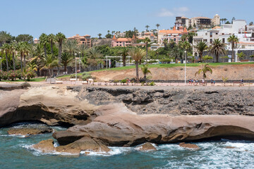 Fototapeta premium Long promenade facing inland towards the parks and gardens, shopping malls and the hotels and residences surrounding the area, Playa del Duque, Costa Adeje, Tenerife, Canary Islands, Spain