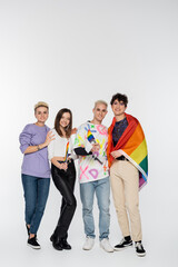 full length of different identity people with lgbtq flags smiling at camera on grey background.