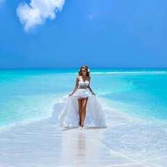 Fototapeta na wymiar Bride on the beach. Stylish female model in elegant long gown dress on the Maldives beach. Elegance. Bride on Maldives. Bridal fashion. Classy woman in amazing ruffle white dress. Luxury travel
