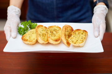 Garlic bread on white plates served by restaurant waiter wearing white gloves for cleanliness and safety.