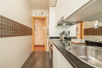 Kitchen with gloss black stone countertops, white cabinets, stainless steel undermount sink, square tiled valance and mirror under cabinets, and matte steel appliances