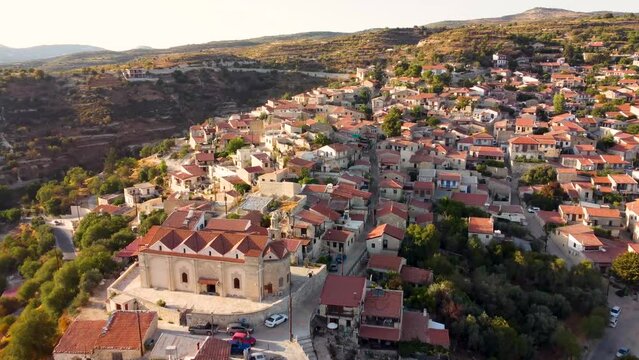 Aerial drone footage of traditional countryside hilltop village Vouni, in Limassol, Cyprus. Establish scene of christian church Ioannis Prodromos, ceramic tiled roof houses, narrow streets from above.