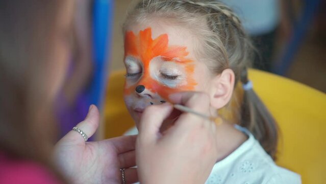 Children face painting. Artist painting with brash and special body paint tiger mask on face of little girl on carnival party for children. Body art painting for childrens.