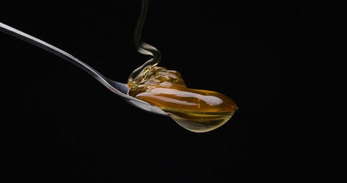 static shot from a spoon is poured over the honey against black background