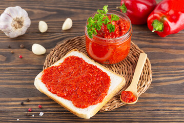 Toast with ajvar from paprika, tomatoes, garlic and onions with spices on a brown wooden table. Balkan food.