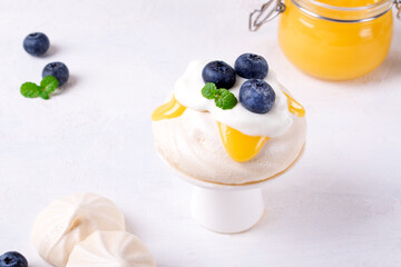 Small Pavlova cake with lemon curd or custard topped with blueberry and mint on white. Meringue dessert