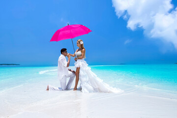 Summer love. Beautiful happy young couple in wedding clothes and pink umbrella is standing on a...
