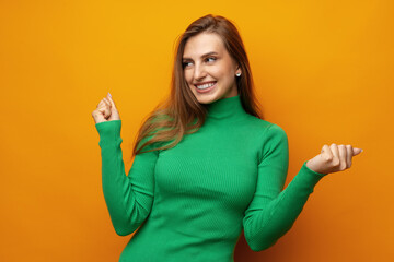Portrait of an excited young woman celebrating success with raised arms against yellow background