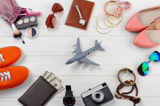 Flat lay mens and womens accessories and toy plane. White wooden desk background.