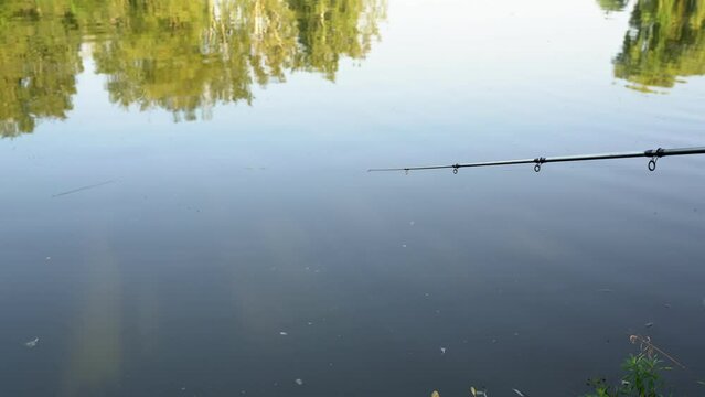 Fishing for pike, perch, carp on beach to the feeder. Man catching fish, pulling rod while fishing from lake or pond. Fisherman with rod, spinning reel on river bank. Sunrise - background wild nature
