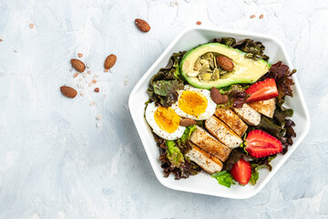 Ketogenic low carbs diet, Plate with keto foods: two eggs, avocado, grilled chicken fillet, nuts, strawberries and fresh salad. Healthy fats, clean eating for weight loss. top view