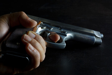 Left human hand holding gun. 9 mm parabellum semi automatic stainless steel pistol lay down on low light dark background. Low key pgotography.