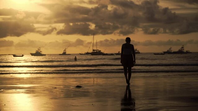 Woman silhouette walking at a beach in Tamarindo in Costa Rica with boats in the background