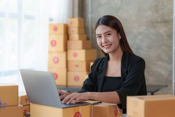 Asian online business owner Prepare parcel boxes for customers. Check the balance and correct shipping address and phone number and save the data using a laptop computer.