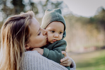 Obraz premium Mother holding and kissing her little baby son wearing knitted sweater during walk in nature, close-up
