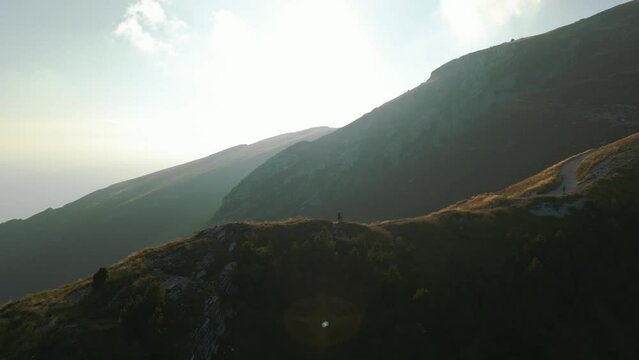 Young happy couple hiking on mountain top in the alps mountains on panoramic Monte Baldo at Garda Lake and Verona in Italy, Valpolicella wine and vinery area sunset, epic cinematic drone aerial view.
