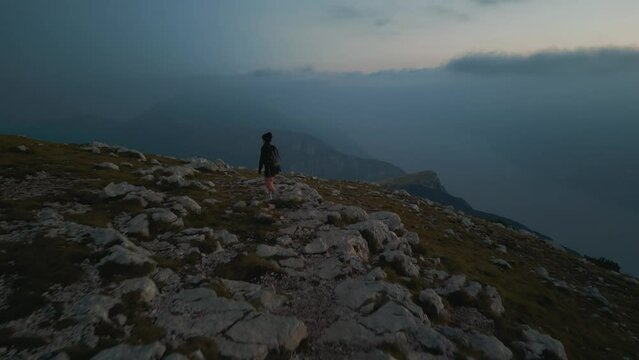 Young sporty girl hiking on mountain top in the alps mountains on panoramic Monte Baldo at Garda Lake and Verona in Italy, healthy fitness sport trekking at sunset, epic cinematic drone aerial evening