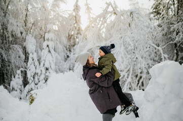 Mother holding her big son in winter nature and enjoying snow.