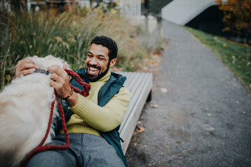 Happy young man training and cuddling with his dog outdoors in city park, during cold autumn day.