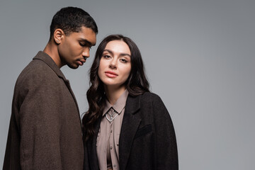 young african american man in coat near stylish woman in blazer isolated on grey.