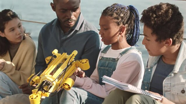Medium slowmo of African American male teacher showing hydraulic centralizer to group of diverse schoolkids during outdoor engineering class