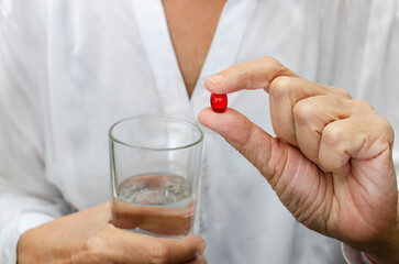 The hand holds a capsule and a glass of water.