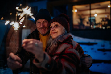 Happy senior couple celebrating new year with sparklers, enjoying winter evening.