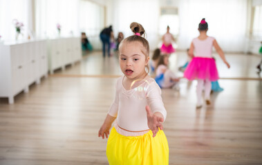 Little girl with down syndrome at ballet class in dance studio. Concept of integration and education of disabled children.