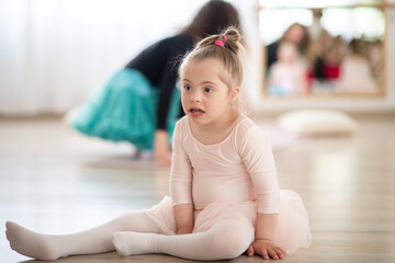 Little girl with down syndrome at ballet class in dance studio,sitting and resting. Concept of...