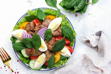 Perigord salad with chicken liver, tomatoes, cucumbers, eggs, lettuce and spinach. Black kitchen table background, top view