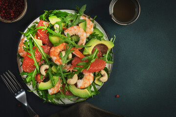 Healthy fresh salad with shrimps, avocado, grapefruit, arugula and cashews. Dark green kitchen  table background, top view, copy space