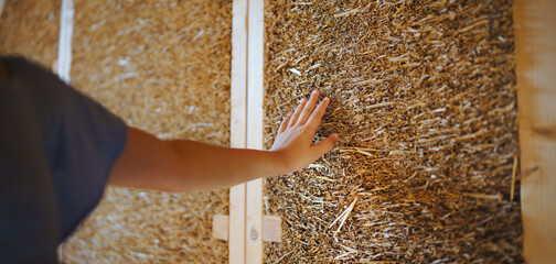 Close-up of girl hand touching straw wooden eco house framing. Concept of sustainability and healthy living.