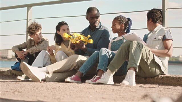Slowmo of African American male teacher giving lesson of engineering to group of smart multiethnic school children, examining hydraulic centralizer outdoors at quay