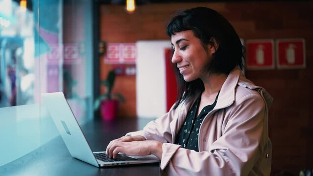 South American happy young woman working in front of laptop at cafe workplace. A Brazilian latina hispanic adult 20s girl typing on computer