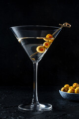 Martini, a glasses with spicy olives on a toothpick, on a black background. Alcoholic cocktail, side view