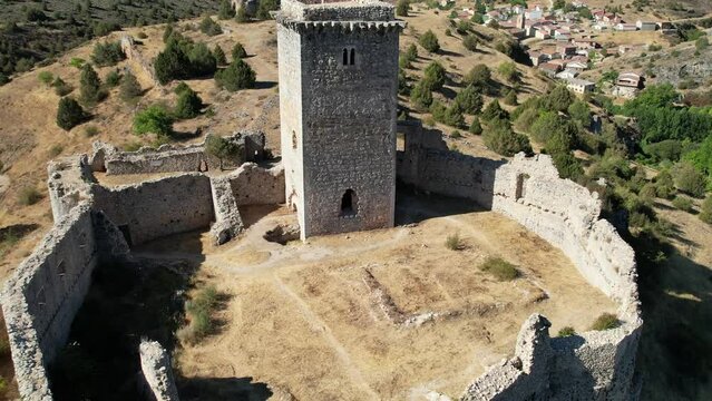 Backward flight view of a medieval tower in a castle in Ucero, Soria (Spain), surrounded by walls, in the top of a hill.