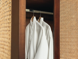 Two white clean bathrobes hanging in wooden wardrobe